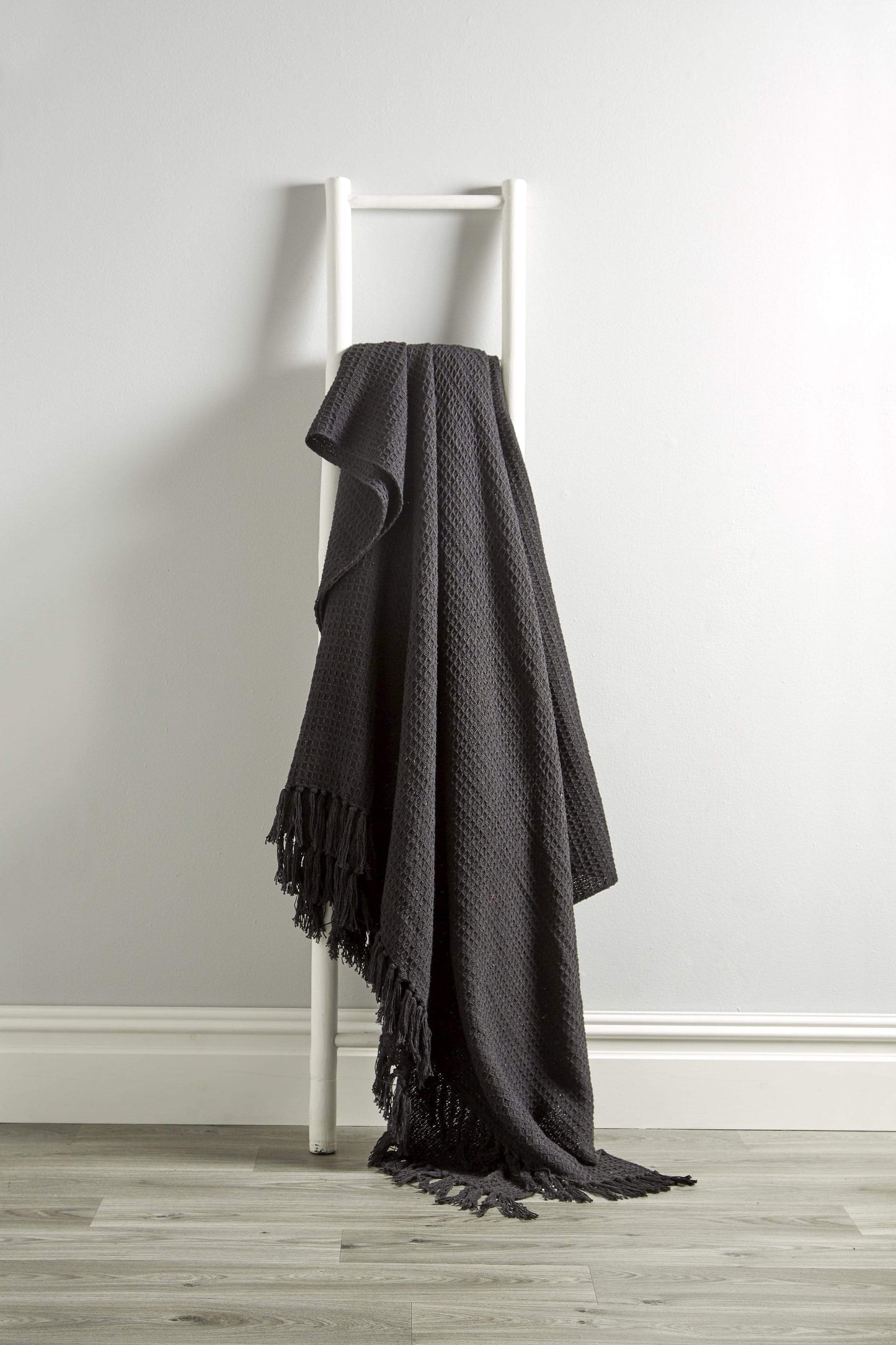 Black blanket draped over a white ladder against a light gray wall.