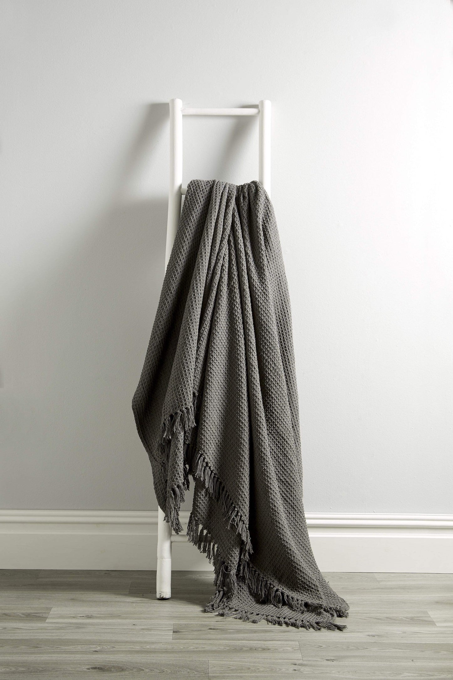 Gray textured blanket draped over a white ladder against a plain wall.