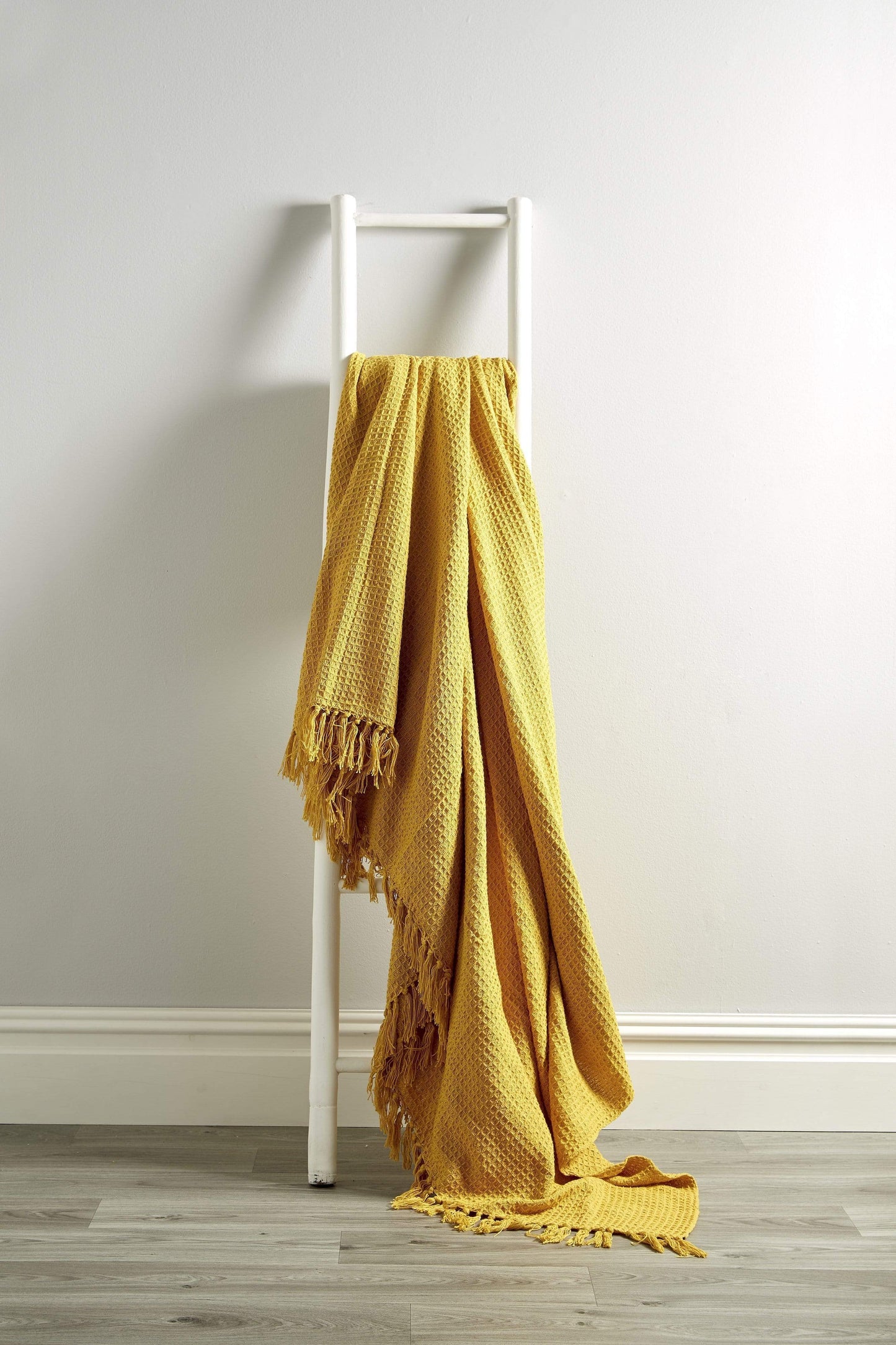Yellow blanket draped over a white ladder against a plain wall.