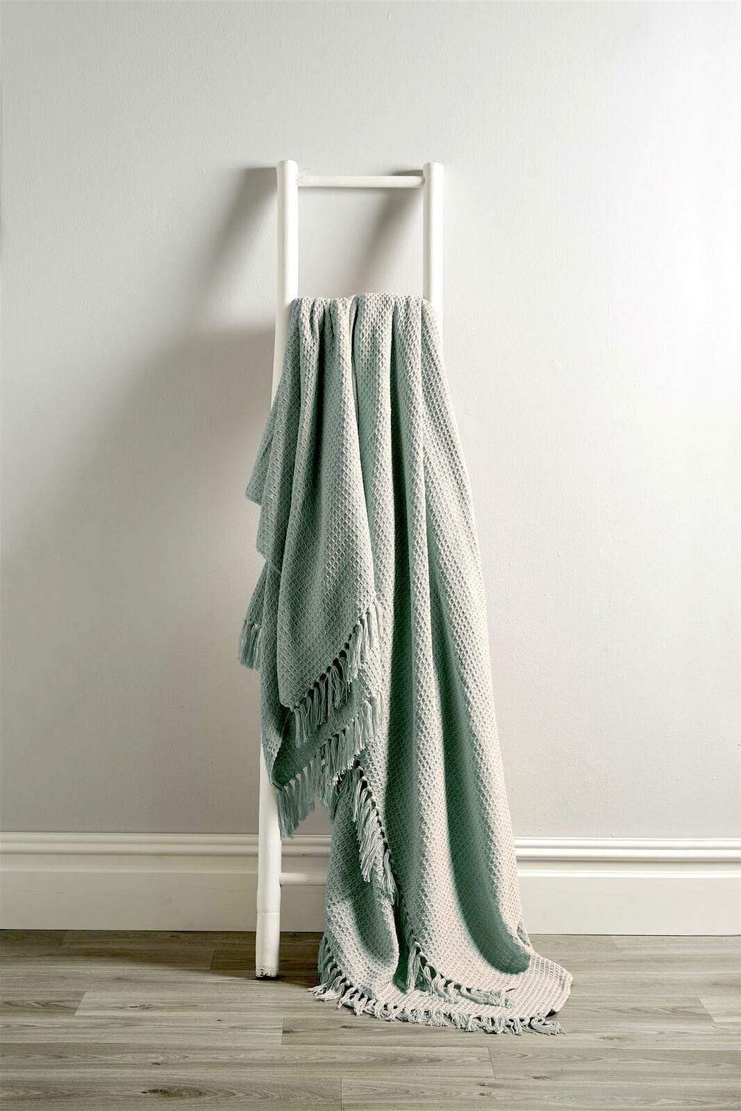 Green blanket draped over a white ladder against a plain wall.