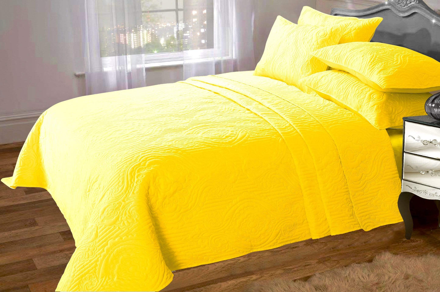 Yellow quilted bedspread on a bed in a room with a window and nightstand.