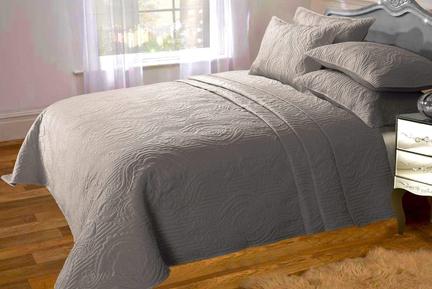 Gray textured comforter on a bed in a bedroom with wooden floor and window.