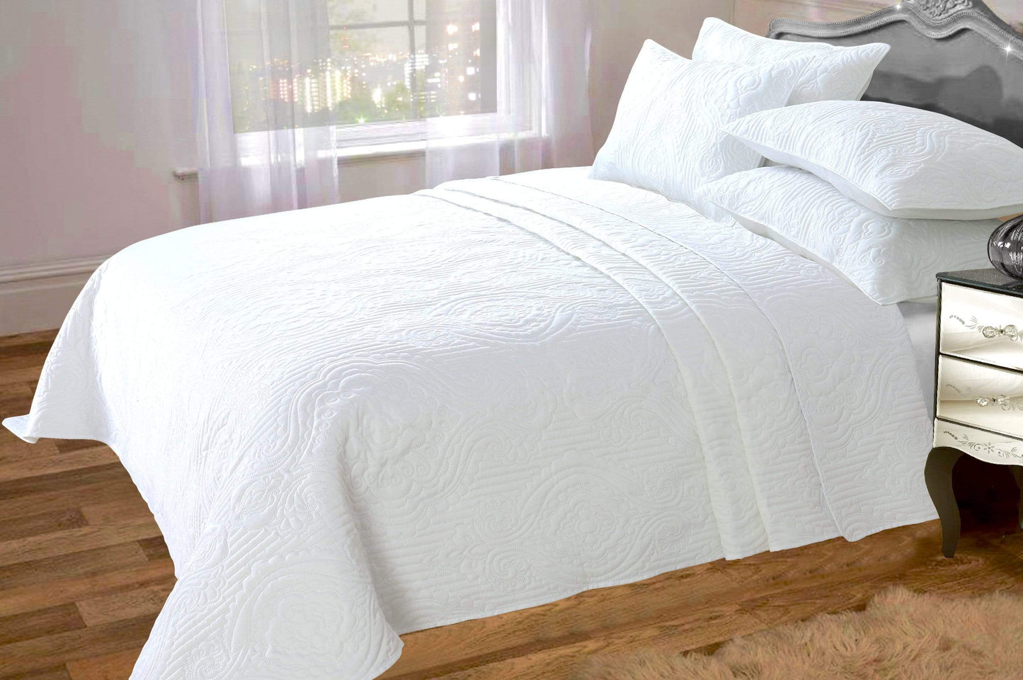 White quilted coverlet on a bed with pillows in a bedroom setting.